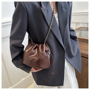 Detail view of dark brown glossy leather bucket bag with chain strap and drawstring closure