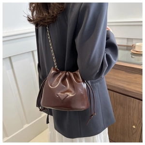 Detail of dark brown drawstring bucket bag with shiny faux leather and gold chain strap