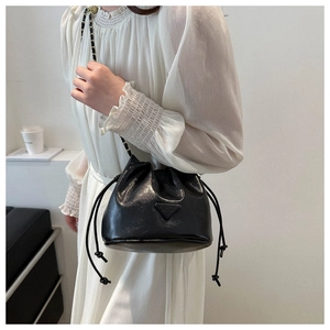 Close-up of black bucket bag with chain strap and glossy finish on white dress