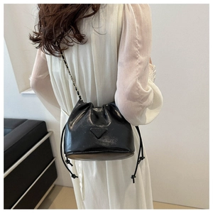 Detail of black bucket bag with chain strap and triangular plaque on white dress