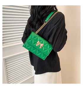 Close-up of green quilted leather crossbody bag with golden bow clasp and chain strap