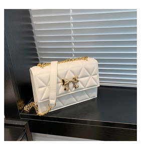 Detail view of a white quilted flap bag with a prominent golden metal bow and chain strap