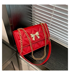 Detail of red quilted faux leather bag featuring a large golden metal bow and chain strap