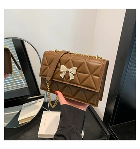 Close-up of brown quilted crossbody bag with golden bow clasp and chain strap