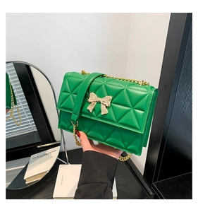Detailed close-up of emerald green quilted crossbody bag with golden bow buckle