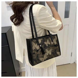 Détail du sac cabas noir élégant avec broderie papillon dorée et pendentif à pompon chic