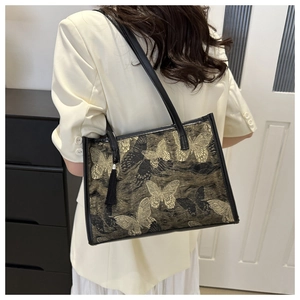 Détail d'un sac cabas en jacquard noir avec broderie papillon dorée et breloque à franges