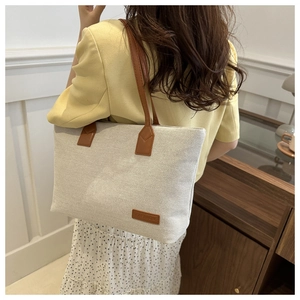 Detail of canvas tote bag with brown leather straps worn by model in a minimalist room