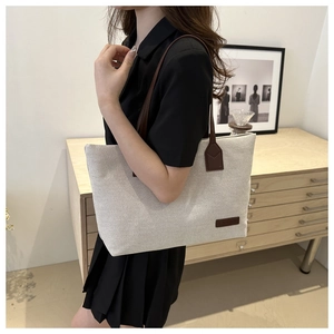 Detail of a large canvas tote bag with brown leather straps in a minimalist lifestyle setting