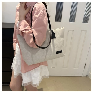 Detailed shot of a large beige canvas tote bag with black straps on a woman's shoulder