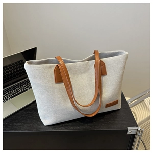 Detail of canvas tote bag showing fabric texture, leather handles, and laptop for scale