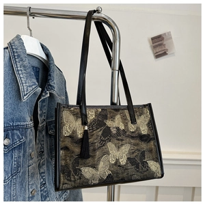 Détail du motif papillon en jacquard et pompon en soie noire sur un sac cabas chic
