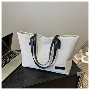 Detail of a beige canvas tote bag with black leather straps and a fashion label