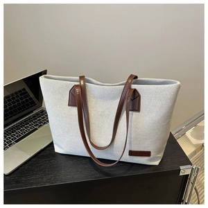 Detail of grey woven texture tote bag with brown leather strap on a modern office desk