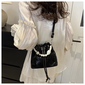 Détail d'un sac seau noir chic à cordon avec une élégante poignée en perles blanches