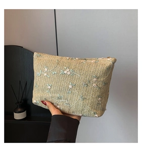 Detailed embroidery on a woven khaki clutch bag with pink floral patterns