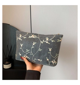 Detail of dark grey embroidered woven clutch with pink floral patterns and gold zipper
