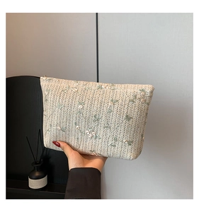 Close-up of beige woven clutch featuring delicate pink floral embroidery and metal zipper detail
