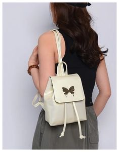 Close-up of a cream butterfly bow backpack featuring a metallic clasp and glossy PU texture