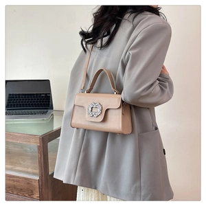 Détail d'un sac à main rectangulaire marron avec boucle en strass élégante sur blazer gris