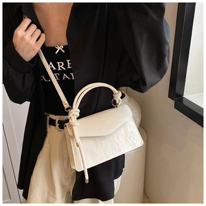 Detail of white pleated handbag with unique knotted handle and adjustable strap