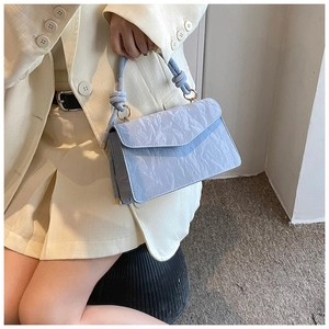 Detail of light blue textured handbag with knot handle held by model in cream suit