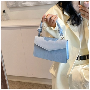 Close-up of light blue leather handbag featuring knotted handle and gold metal rings