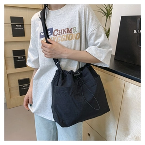 Detail of a black drawstring crossbody bag showing adjustable strap and large front pocket