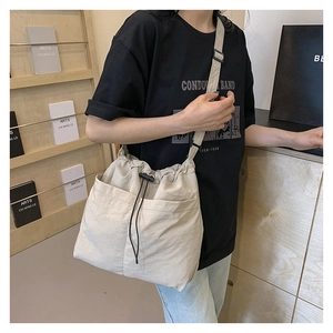 Adjustable crossbody strap and front drawstring pockets on a beige large nylon tote bag