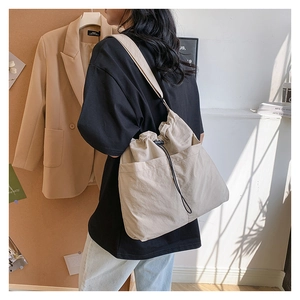 Detail of beige drawstring tote bag featuring two large front pockets and nylon texture