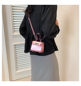 Mini metallic pink crossbody bag with silver lock and handle shown on a black outfit