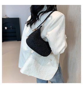 Close-up of black glitter crescent underarm bag with gold hardware on white blazer