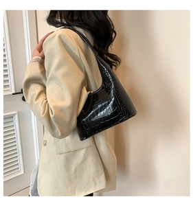 Détail d'un sac à main noir à motif crocodile porté avec un blazer beige chic