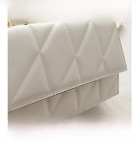 Detail shot of white quilted shoulder bag with fine stitching and gold chain strap
