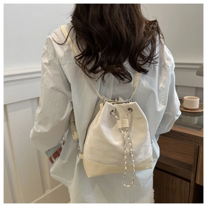 Chic beige bucket backpack with silver chain detail shown on model in a cozy indoor setting