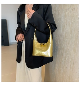 Détail du sac à main doré avec gaufrage crocodile porté élégamment à l'épaule