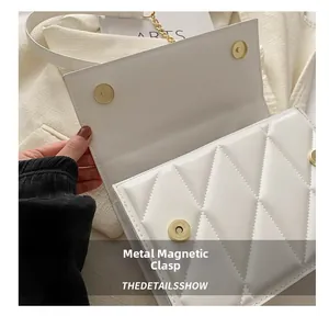 Detailed macro shot of the golden magnetic closure on a white quilted leather flap bag