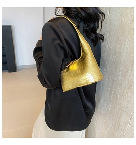 Détail d'un sac sous le bras doré à motif crocodile porté par un mannequin