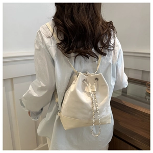 Rear view of a model wearing a stylish off-white drawstring backpack with silver chain
