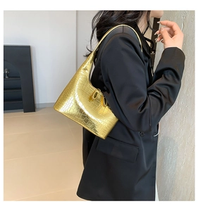 Détail d'un sac hobo doré à motif crocodile porté par un mannequin en costume noir élégant