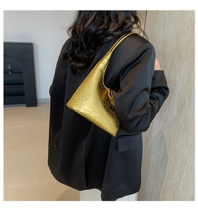 Gros plan du sac hobo doré à motif crocodile porté à l'épaule sur un blazer noir