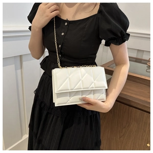 Close-up of a white quilted crossbody bag with gold chain strap on a black dress