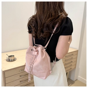 Pink drawstring bucket backpack with stylish chain strap worn by a model in a cozy setting