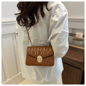 Sac bandoulière matelassé marron avec chaîne dorée porté par un mannequin en café