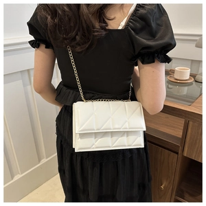 Detailed view of a white quilted crossbody bag with gold chain strap on a model