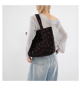 Dettaglio di una borsa tote in velluto nero con motivi a fragola sulla spalla di donna