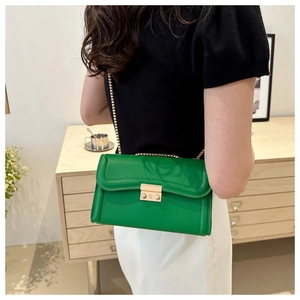 Gros plan d'un sac bandoulière vert à chaîne dorée porté par un mannequin féminin