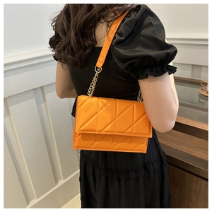 Orange quilted shoulder bag with chain strap styled with a black dress back view