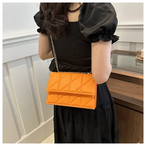 Close-up of vibrant orange quilted crossbody bag with gold chain strap on model