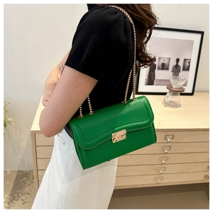 Détail du sac à bandoulière en cuir vert avec chaîne dorée et fermoir rond sur le modèle